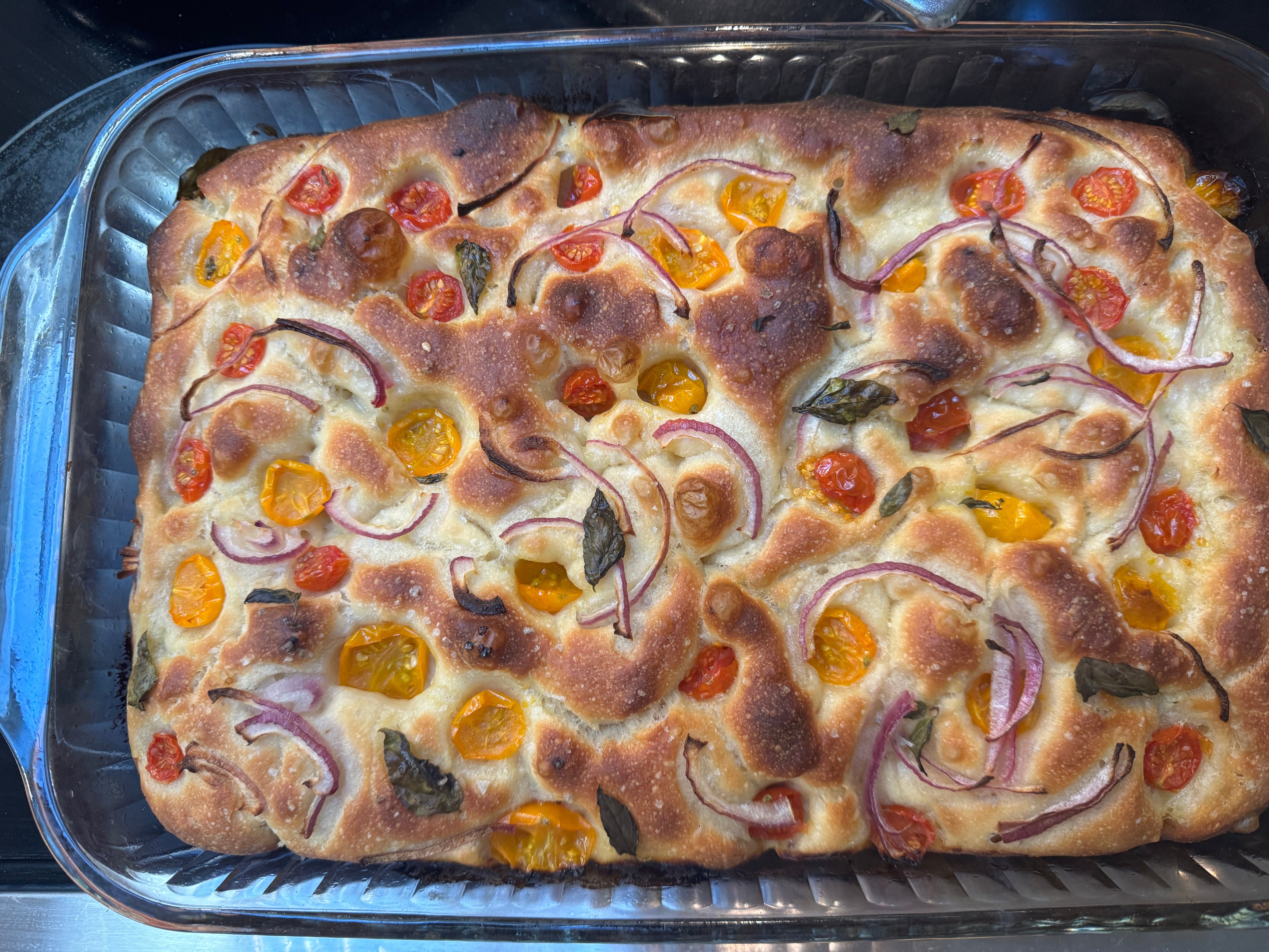 Baked focaccia bread with tomatoes and onions in a baking tray